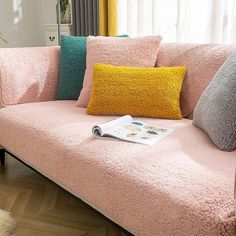 a pink couch with several pillows on it in front of a window and a rug