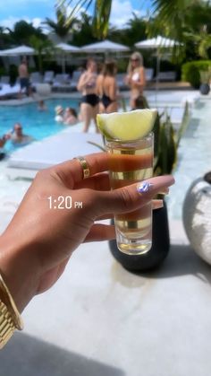 a woman holding up a glass with a lemon slice on it in front of a swimming pool