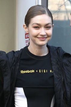 a woman in a black shirt and white pants smiles at the camera while standing outside