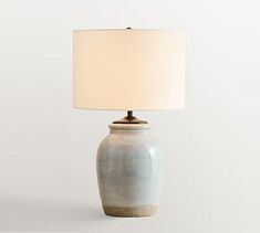 a table lamp with a white shade on it and a light blue vase in the middle