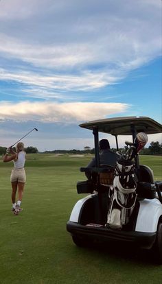 a woman is playing golf on the green with a cart in front of her and a man standing next to her