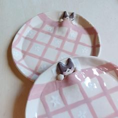 two pink and white plates with small figurines on them sitting on a table