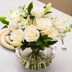 a vase filled with white flowers sitting on top of a table next to a plate