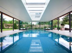 an indoor swimming pool with skylights and lounge chairs around the perimeter, surrounded by glass walls