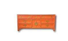 an orange dresser with gold handles and knobs on the drawers is against a white background