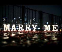 the word marry me is lit up in front of a cityscape at night