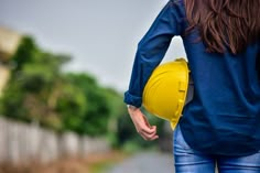 a woman in jeans and a yellow hard hat walks down the street with her back to the camera