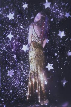 a woman standing in front of stars wearing a gold dress