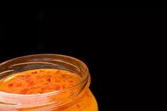 a glass jar filled with orange liquid on top of a wooden table next to a black background