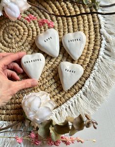 four white heart shaped cookies sitting on top of a woven table cloth next to flowers