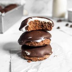 three chocolate covered cookies stacked on top of each other next to a glass of milk