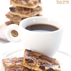 three pieces of pecan bar sitting on top of a white plate next to a cup of coffee