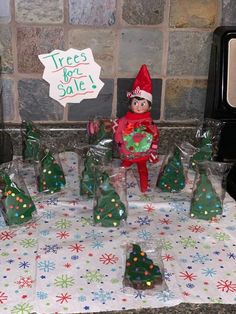 an elf is holding a christmas tree in front of some small trees on a table