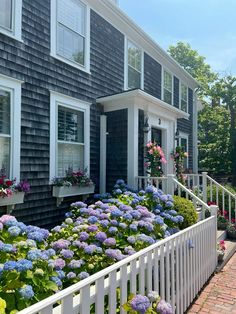 a house with flowers in front of it and a white picket fence around the yard