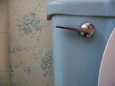 a blue toilet in a bathroom with floral wallpaper