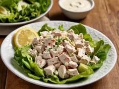 a salad with chicken and lettuce on a white plate next to a bowl of dressing