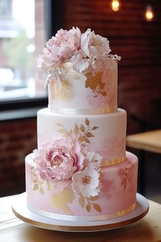 a three tiered wedding cake with pink and gold flowers on the top, sitting on a wooden table