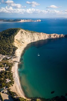 an aerial view of the beach and ocean with sailboats in the water, surrounded by green trees