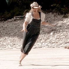 a woman wearing overalls and a hat running