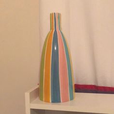 a multicolored vase sitting on top of a white shelf next to a curtain