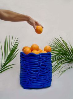 a hand reaching for an orange in a blue container