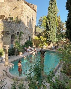 an outdoor swimming pool in front of a stone building with trees and bushes around it