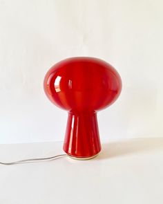 a red table lamp sitting on top of a white counter next to a light bulb