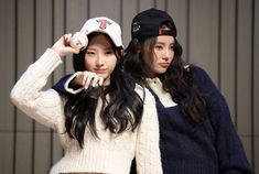 two young women standing next to each other with baseball caps on their heads and one wearing a white sweater