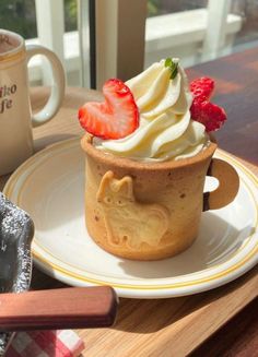 a cup with whipped cream and strawberries in it on a plate next to a window