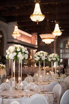 the tables are set with white flowers in tall vases and candles on each table