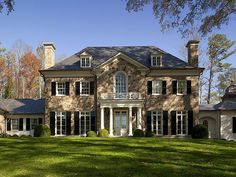 a large brick house sitting in the middle of a lush green field with lots of trees