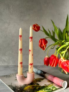 two candles sitting on top of a magazine next to red flowers and tulips