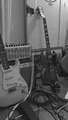 two electric guitars are sitting on the floor next to an amplifier and guitar case in black and white