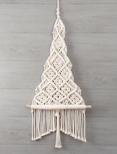 a white macrame christmas tree hanging on a wooden wall in front of a gray background