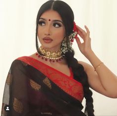 a woman wearing a red and black sari with gold jewelry on her neck, standing in front of a white backdrop