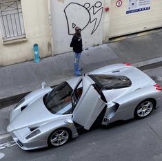 a man standing next to a silver sports car on the side of a road with its door open