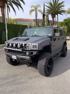 a black hummer truck parked in a parking lot with palm trees and bushes behind it