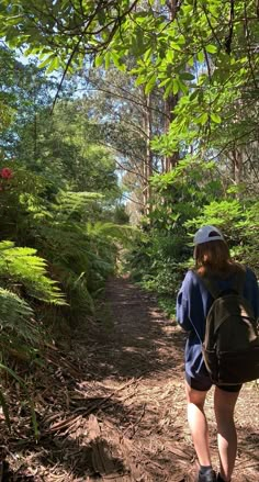 a woman with a backpack walks down a path in the woods on a sunny day