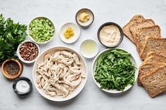 an assortment of food including bread, vegetables and dips on a white table top