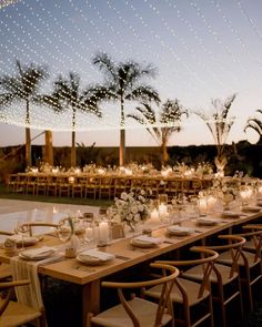 a long table is set with candles and flowers for an outdoor wedding reception at dusk