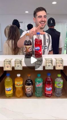 a man pointing at bottles of soda in front of him and another person standing behind the counter