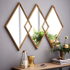 three mirrors are hanging on the wall above a table with a vase and flowers in it