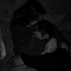 a woman hugging a young boy on top of a bed in the dark with his arm wrapped around him