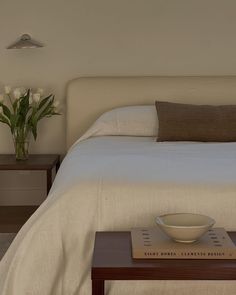 a bowl on a table in front of a bed with white linens and pillows