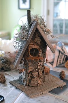 a birdhouse made out of wood and hay on top of a table with pine cones