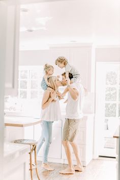 a man and woman are standing in the middle of a kitchen with two children on their shoulders