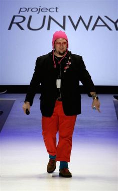 a man walking down a runway wearing red pants and a black jacket with a pink hoodie on