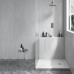 a white bathroom with marble flooring and walls, along with a glass shower door