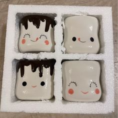 four square dishes with faces painted on them in the shape of marshmallows