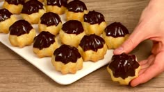 a person is picking up some chocolate covered cookies on a white plate with a wooden table in the background